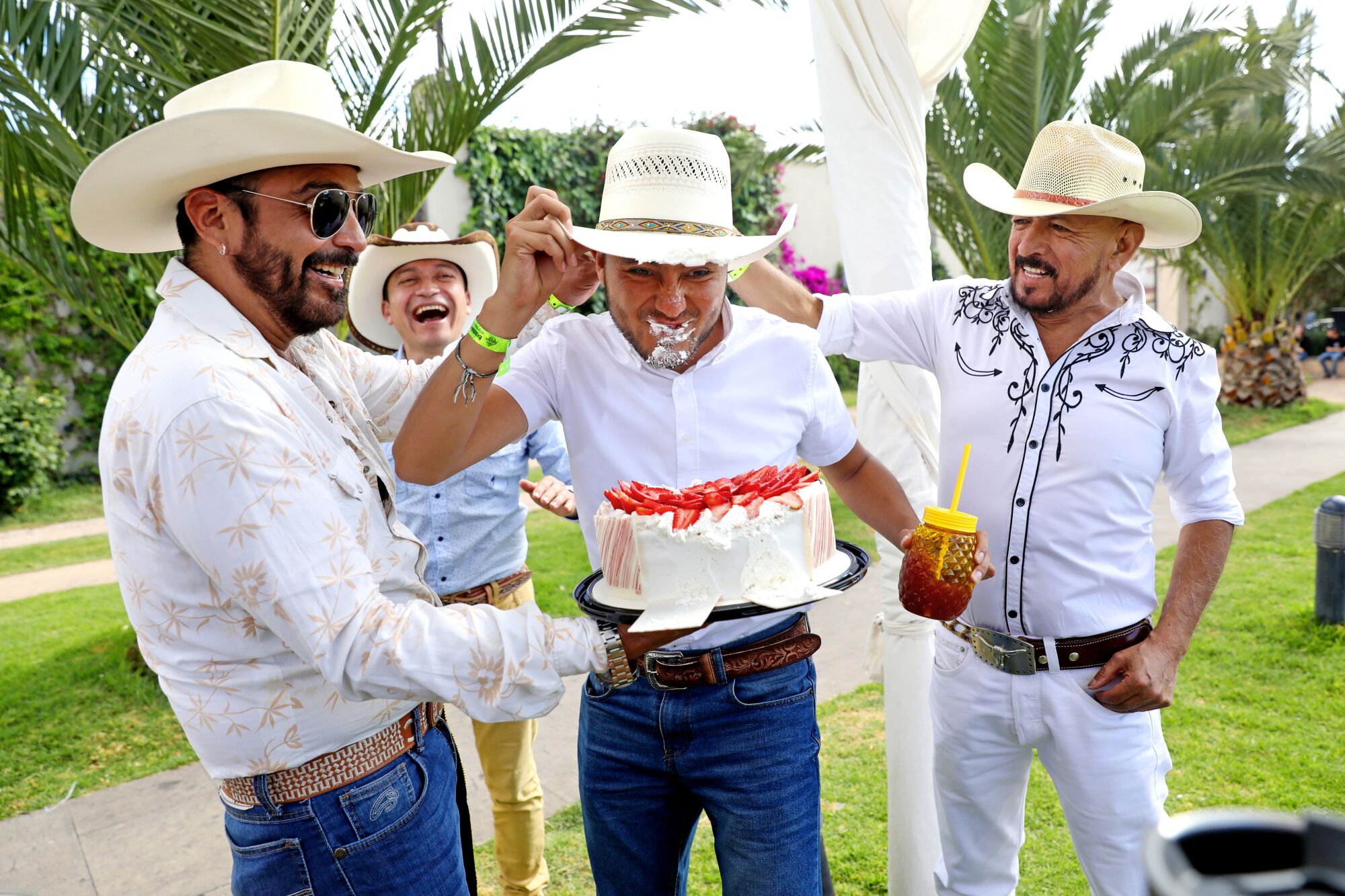  Men in cowboy hats present a friend with a birthday cake. 