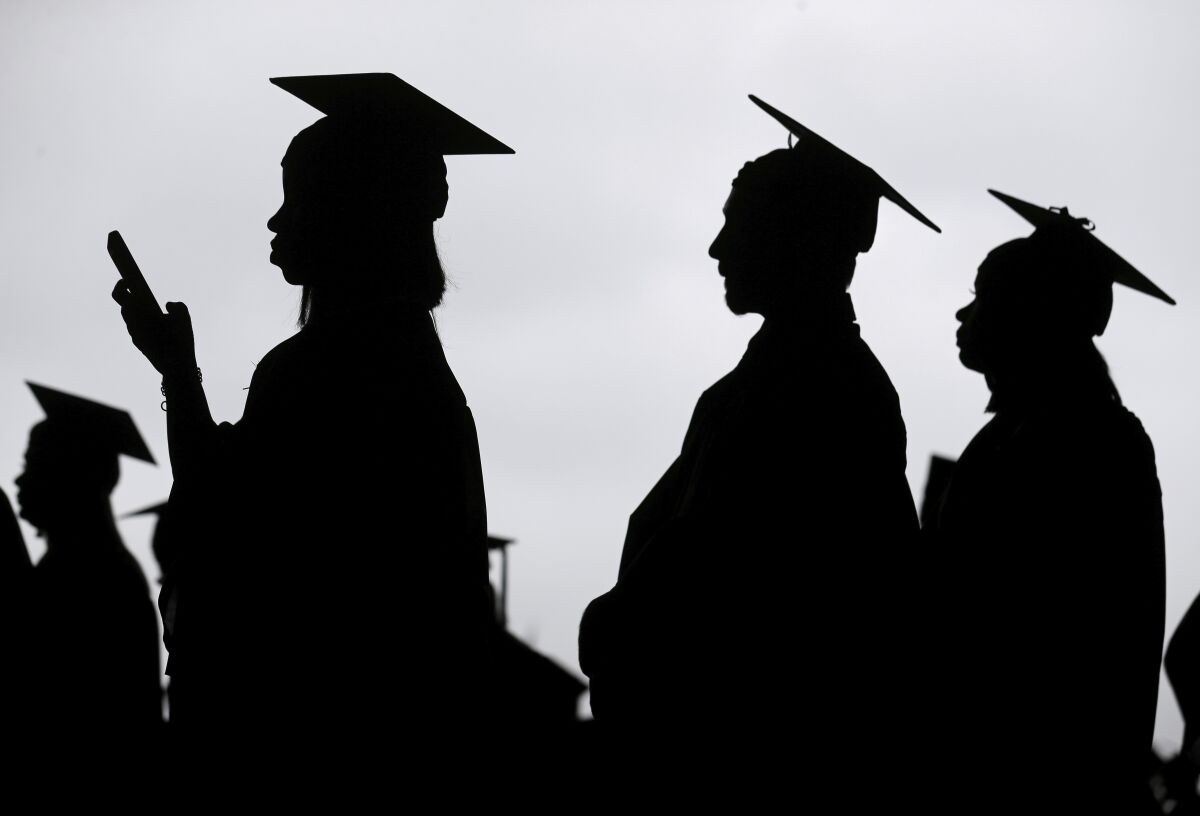 Graduates standing in cap and gown are seen in silhouette