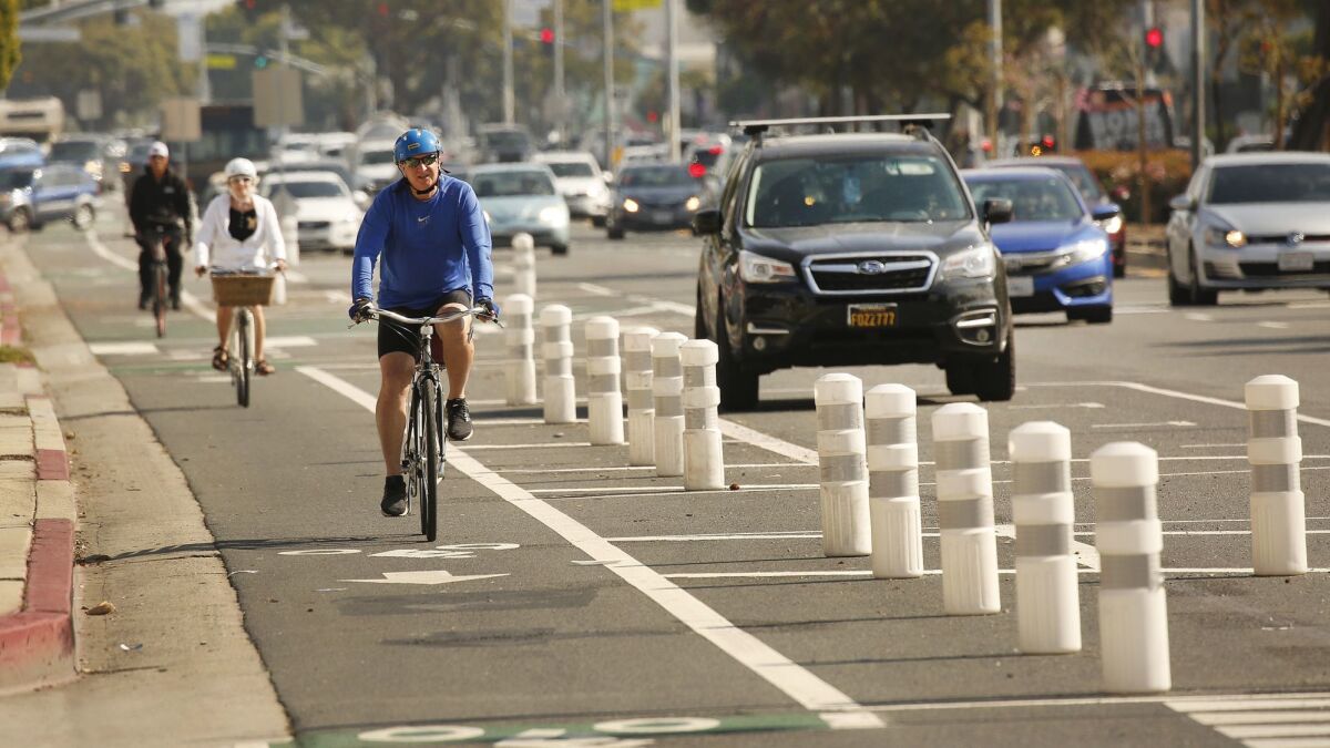 Los Angeles, CA - MARCH 5, 2019 Cyclists navigate the west bound lanes of a new temporary and controversial bike lane along Venice Boulevard in Mar Vista Tuesday March 5, 2019.The curbside lane is marked by plastic pylons buffered by parked cars and is slated to become permanent after today's City Council meeting. The bike lane ignited controversy, and an unsuccessful recall attempt against Westside Councilman Mike Bonin, after city officials removed a lane of traffic to install it, creating a safer way to bike through the neighborhood but sparking some traffic delays on a major arterial. (Al Seib / Los Angeles Times)