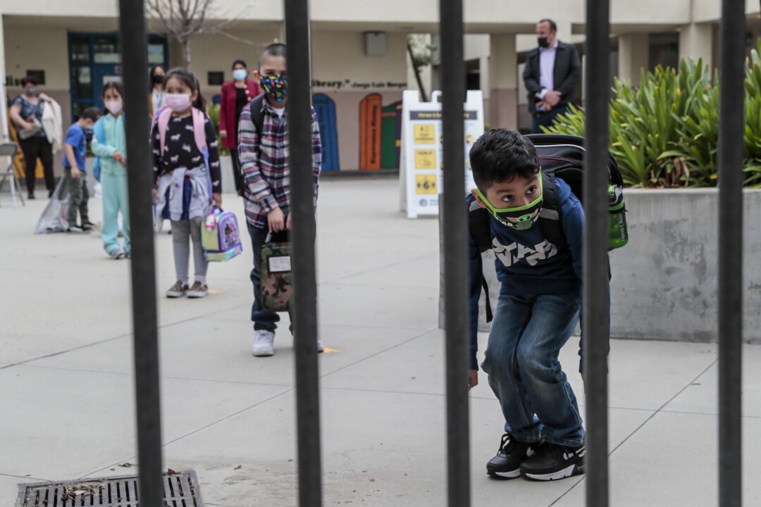 Photos: Tears and cheers after more than a year as LAUSD
resumes in-class instruction 7 A boy in a mask and backpack bends and peeks through a gate.