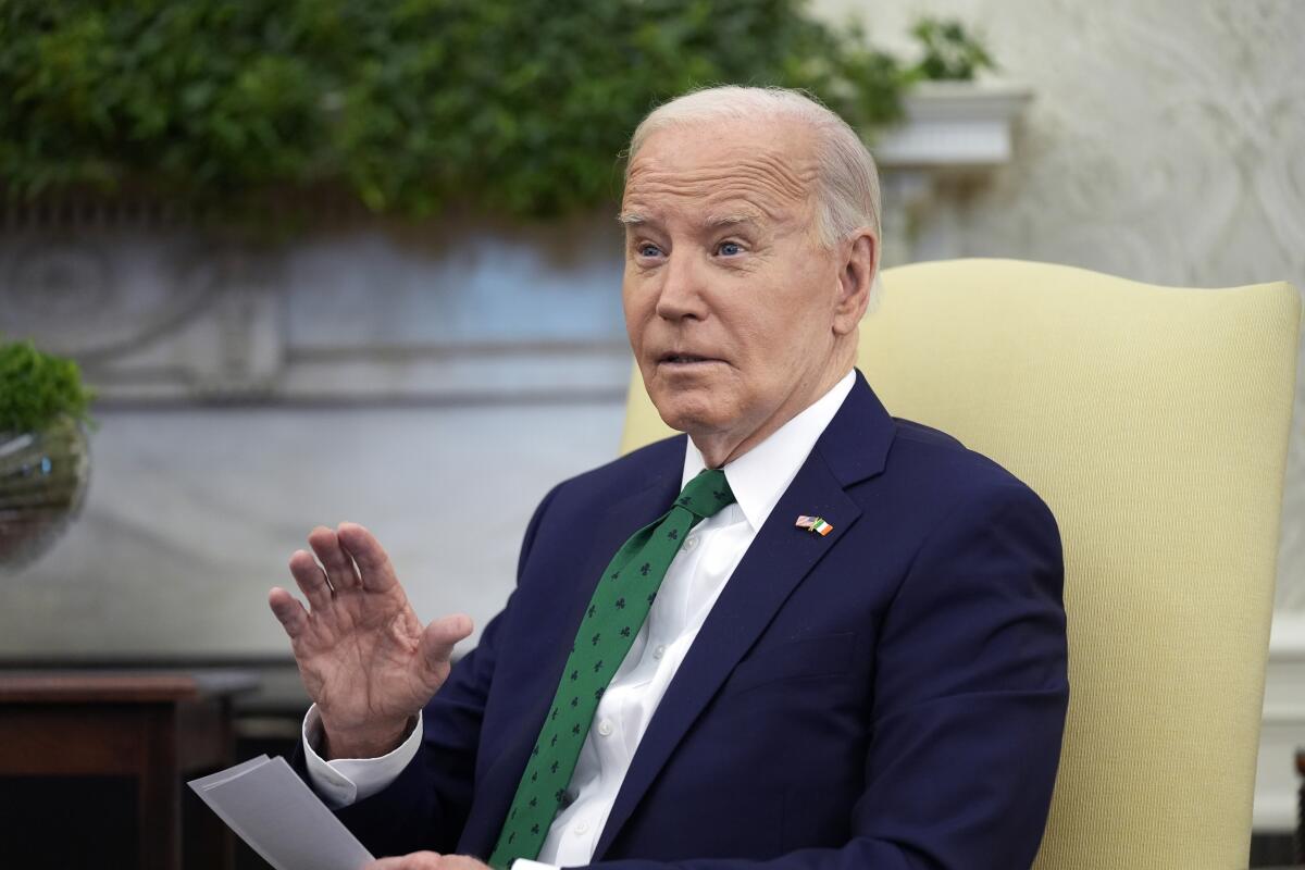 President Biden, wearing a green tie, gestures while seated and speaking 
