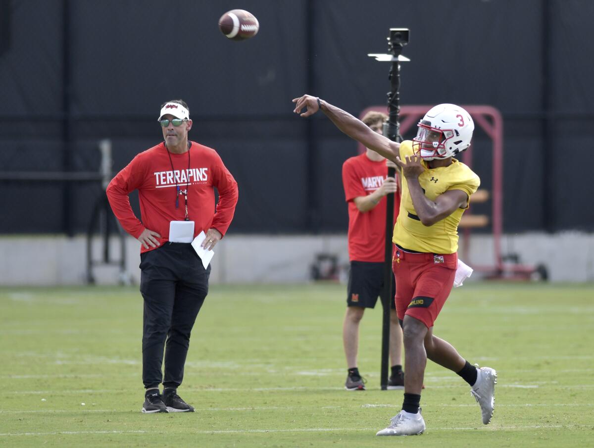 Maryland quarterback Taulia Tagovailoa, right, passes as offensive coordinator Dan Enos, left, watches during the team's NCAA college football practice, Wednesday, Aug. 3, 2022, in College Park, Md. (AP Photo/Steve Ruark)