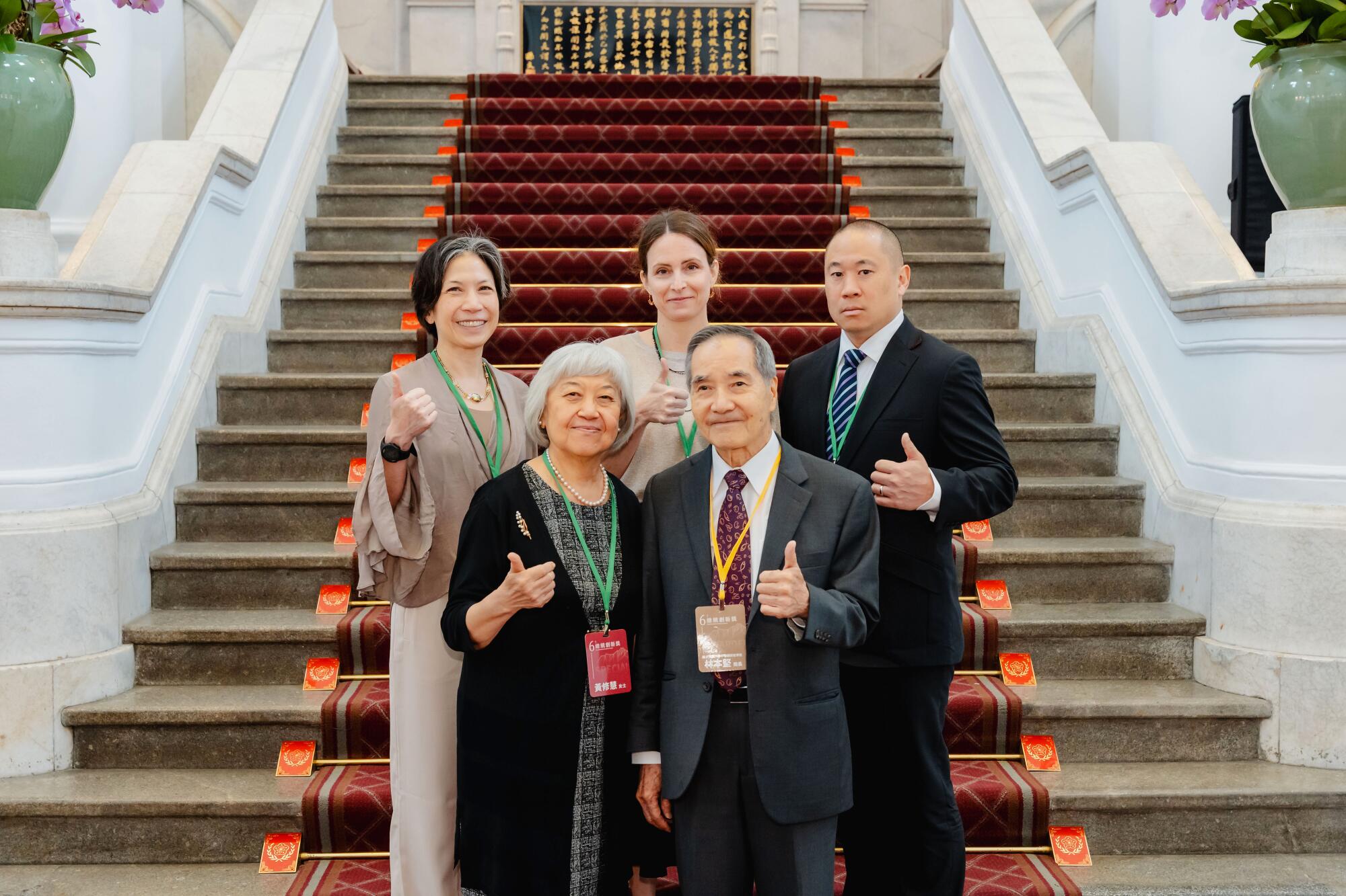 Taiwan - Burn Lin with several people giving a thumbs up as they stand at the bottom of a carpeted staircase.