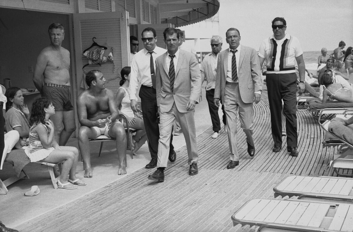 Singer and actor Frank Sinatra, with his minders and his stand-in, who is wearing an identical outfit. The group walked the boardwalk at the Fontainebleau Miami Beach while filming the 1968 film "The Lady In Cement."