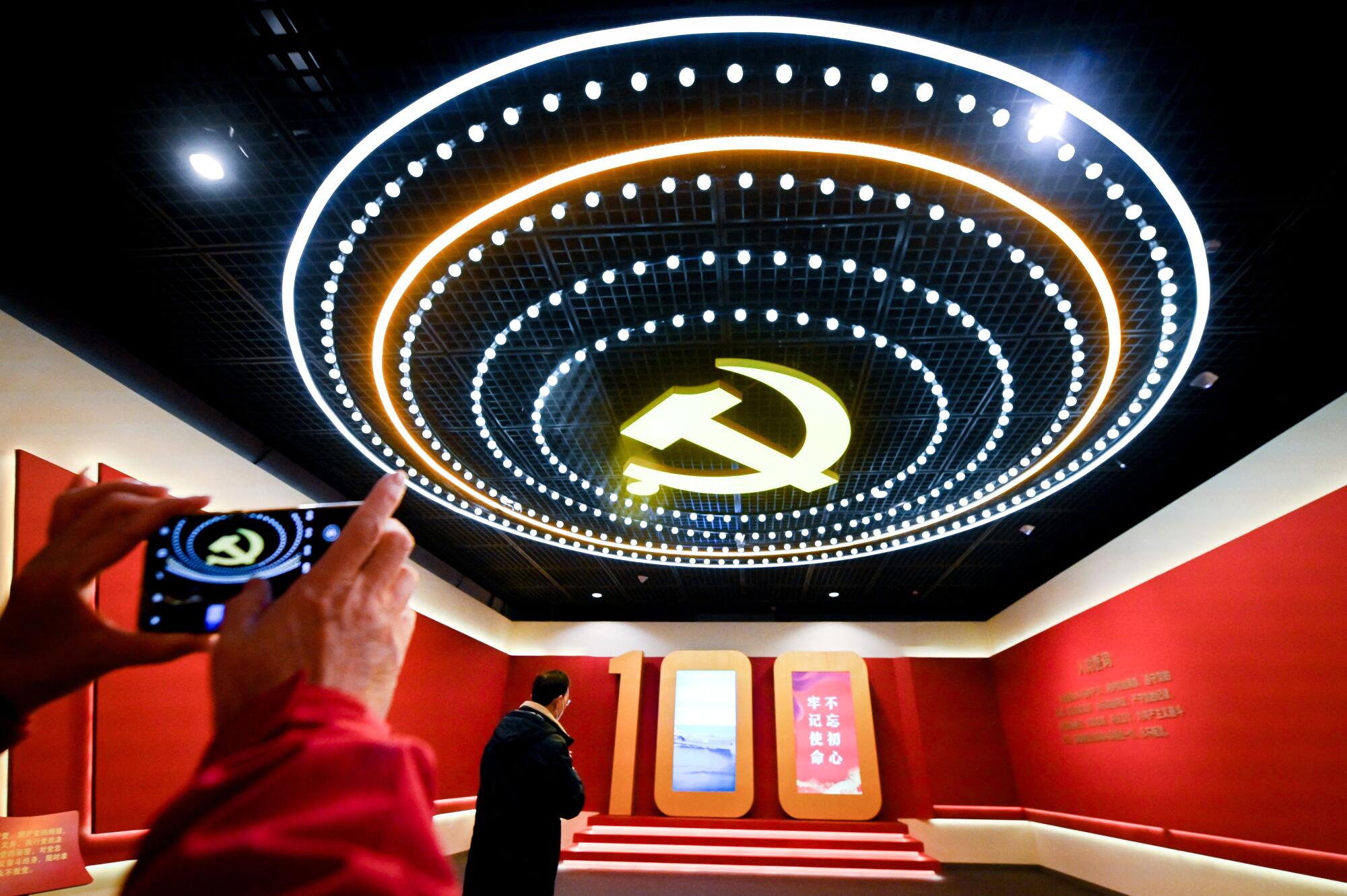 A hammer and sickle logo on the ceiling is ringed by lights in a red room