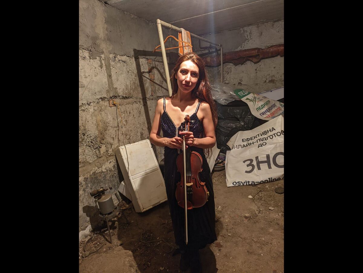A woman stands with a violin in a basement.
