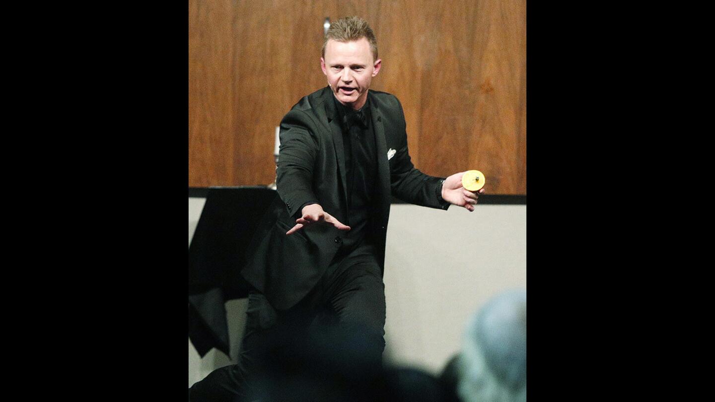 Comedian and magician Joel Ward, after creating the illusion of burning a woman's $20 bill that a small girl colored on, finds the missing bill in an orange at Family Night featuring comedian and magician Joel Ward at the Buena Vista branch of the Burbank Central Library on Wednesday, January 31, 2018. About 50 children and their parents were in the audience