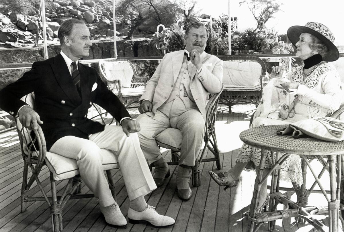 David Niven, left, Peter Ustinov and Bette Davis seated on on a patio in “Death on the Nile” (1978)