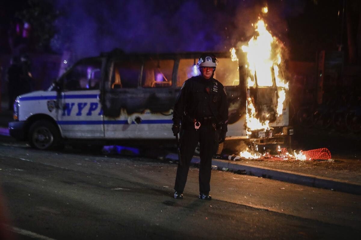 A police officer watches a crowd as a police vehicle burns near Fort Greene Park in the Brooklyn borough of New York 