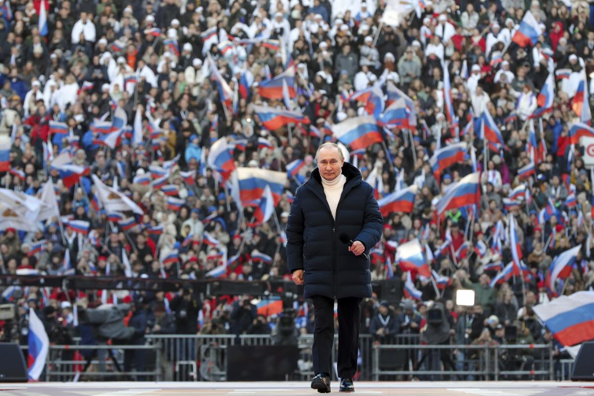 Russian President Vladimir Putin walks before a crowd of people waving Russian flags.