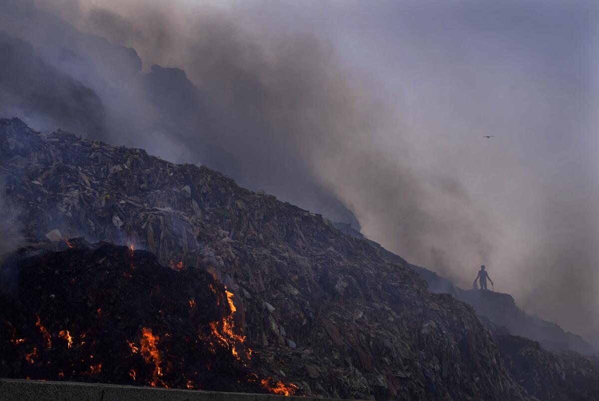 A person picks through trash for reusable items as a fire rages at the Bhalswa landfill in New Delhi. 