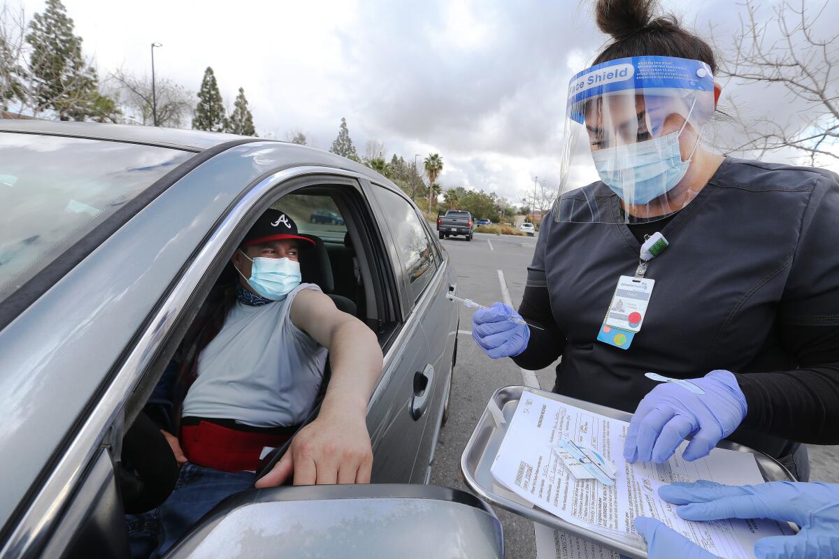 A man waits in a car with his sleeve rolled up as a woman holds a syringe.