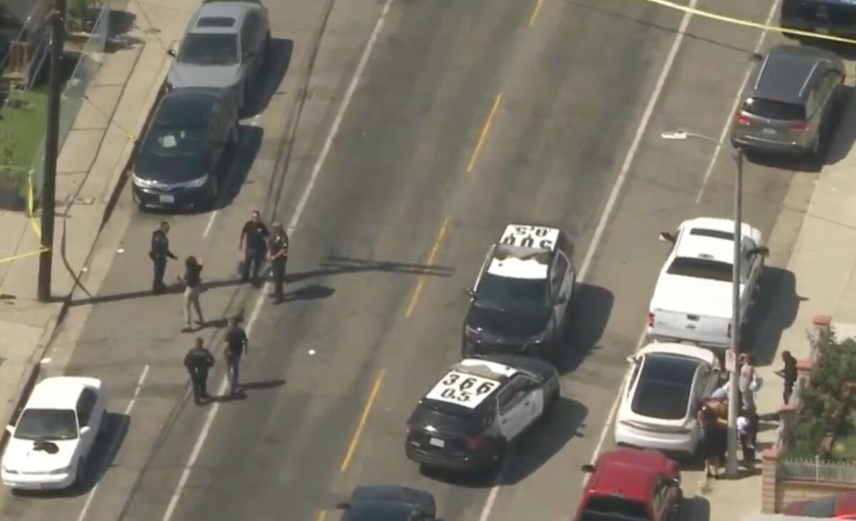 Officers and police cruisers on a street near crime scene tape.