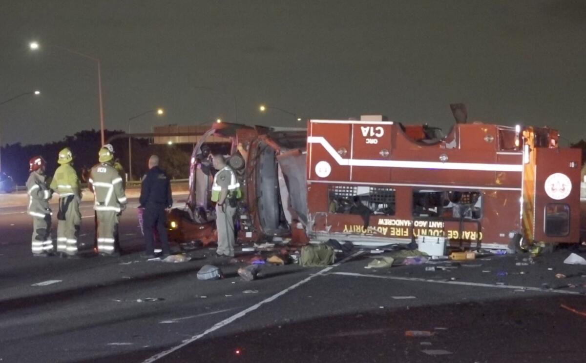 Firefighters stand next to an overturned firefighting vehicle on a highway at night 