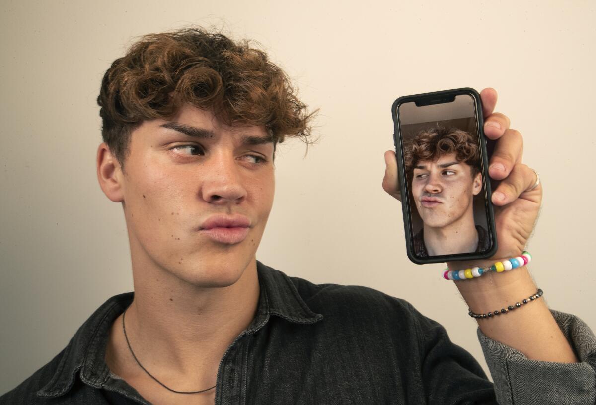 TikTok influencer Noah Beck holds up a cellphone with an image of himself on the screen