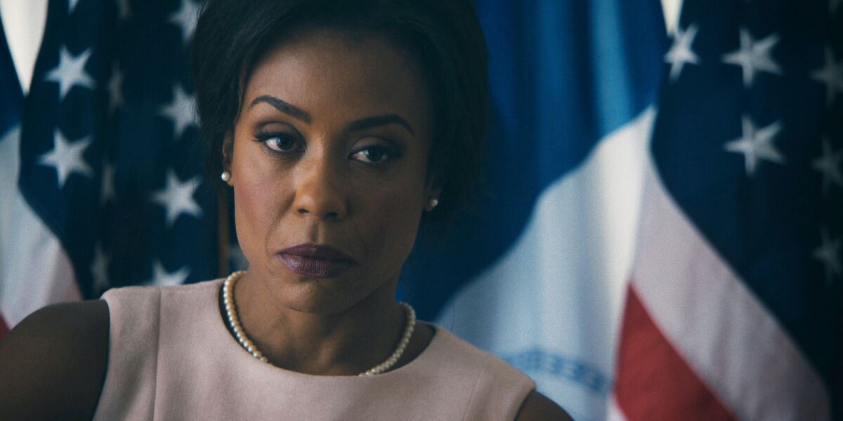 A serious-looking woman stands before several national flags