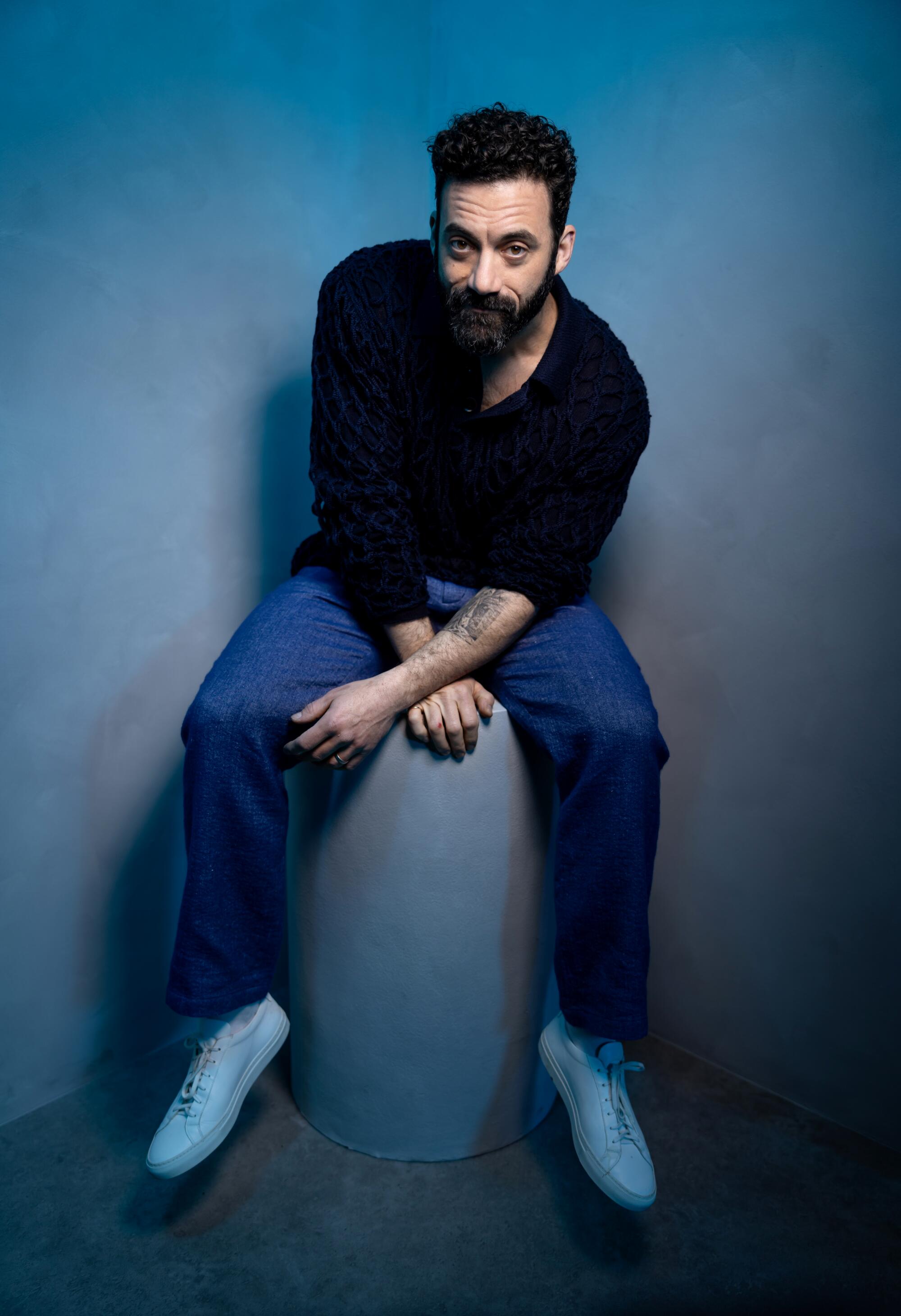 Morgan Spector sits on a pedestal and leans forward for a portrait.