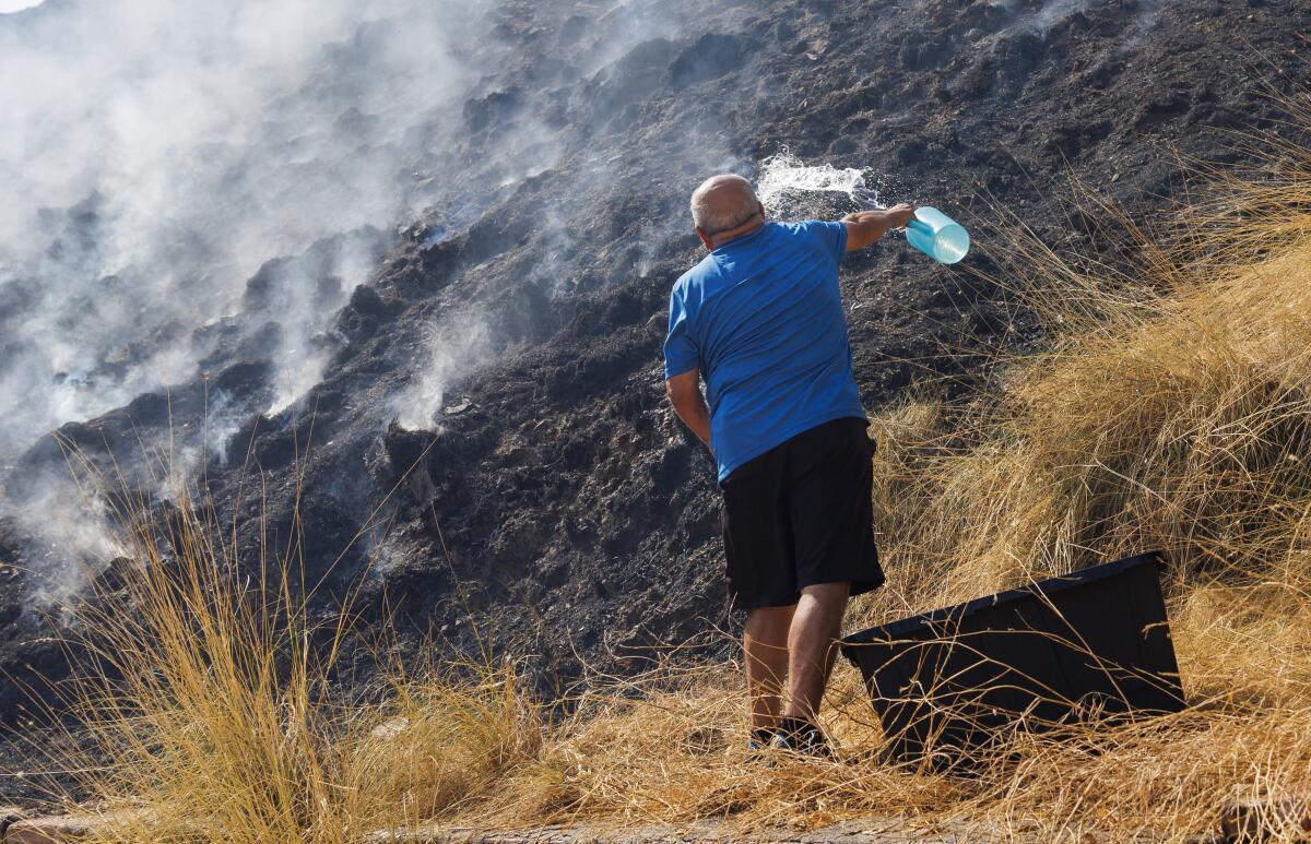 A man is seen from the back next to smoking, charred ground.