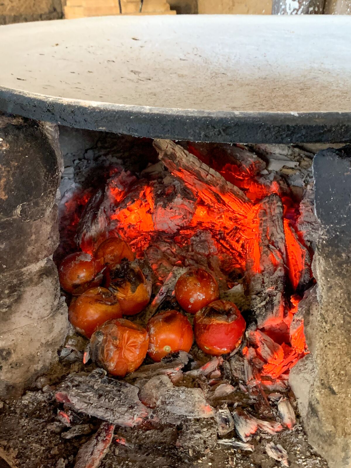 Tomatoes for the mole roast in the coals below the comal.