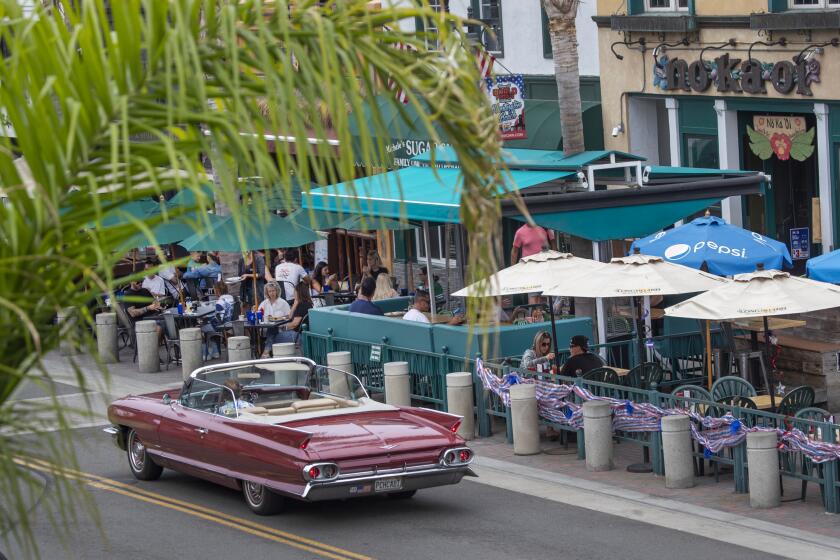 HUNTINGTON BEACH, CA - JULY 01: A classic convertible passes by patrons dining at restaurants and bars on Main Street Wednesday, July 1, 2020 in Huntington Beach, CA. Bars across Orange County, many of which have only recently reopened, will be forced to shut down again beginning at midnight Thursday, Gov. Newsom announced. County officials on Wednesday announced the closure of bars, pubs, breweries and brewpubs that do not offer dine-in meals amid a troubling surge in coronavirus cases that has resulted in an increased hospitalization rate and the placement of the county on Gov. Gavin Newsom's watch list. (Allen J. Schaben / Los Angeles Times)