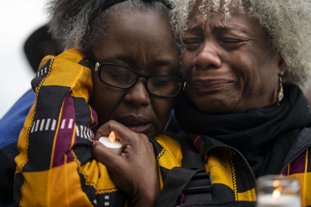 A closeup of the faces of two Black women, one crying and holding a candle in one hand as the other comforts her. 