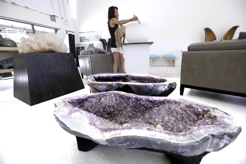 MALIBU, CA - JULY 20, 2021 - - Lenise Soren, owner of Sorenity Rocks, sings as she creates a tone from a quartz crystal singing bowl inside the crystal sanctuary that features pieces for sale from her Sorenity Rocks crystal collection in Malibu on July 20, 2021. A pair of amethyst museum quality tubs or tables rest in the foreground. All items are for sale. The rich are collecting enormous crystals - 7-foot-tall rocks, amethyst thrones, etc. - for their homes. Retail stores and dealers say these status crystals can cost in the hundreds of thousands of dollars and are becoming more popular thanks to Instagram and TikTok. (Genaro Molina / Los Angeles Times)