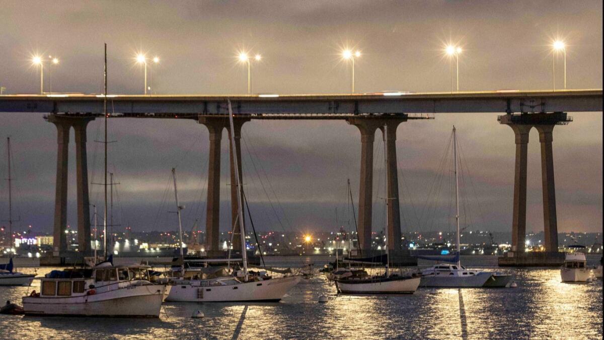 Boats are anchored next to San Diego's Coronado Bay Bridge at dusk.