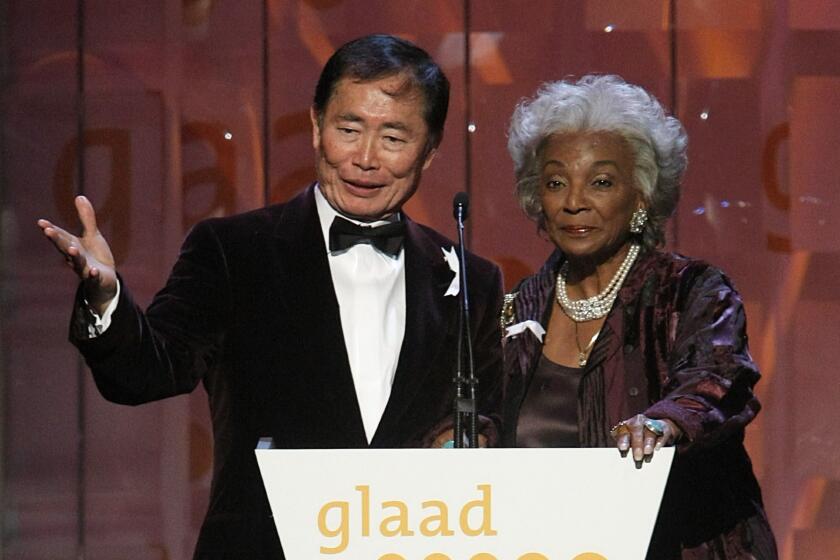 A man in a tuxedo and a woman in purple formalwear standing behind a podium that reads "glaad"