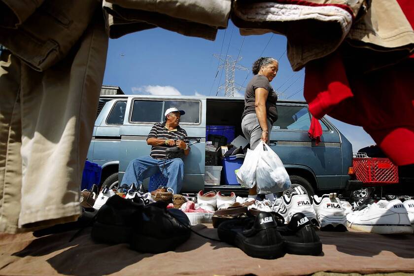 Jesus Navarro, left, looks on as a customer examines the wares in his outdoor vending area in Watts. Los Angeles County officials are looking for ways to crack down on the proliferating informal flea markets.