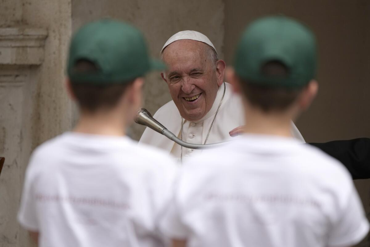 Pope Francis smiles at two children in baseball hats.