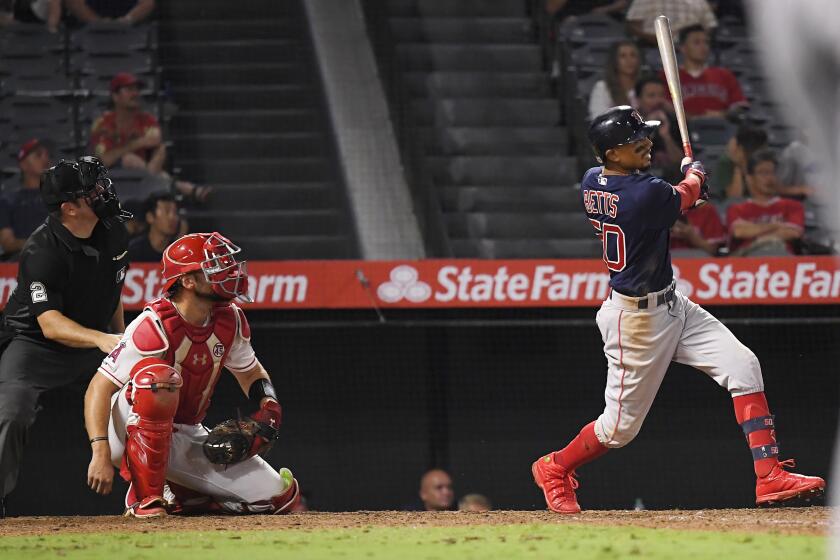 Boston Red Sox's Mookie Betts, right, hits a solo home run as Los Angeles Angels catcher Max Stassi, center, watches along with home plate umpire Dan Bellino during the 15th inning of a baseball game Saturday, Aug. 31, 2019, in Anaheim, Calif. (AP Photo/Mark J. Terrill)