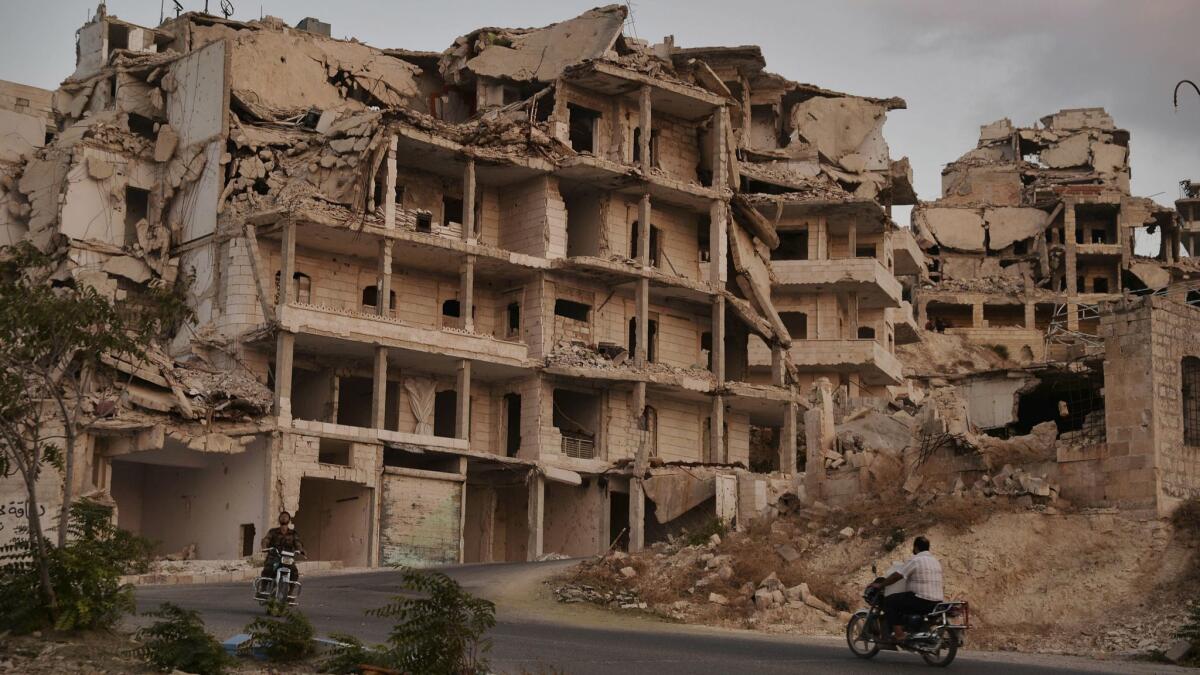 Motorcyclists ride past buildings destroyed during fighting in the northern town of Ariha, in Idlib province, Syria.