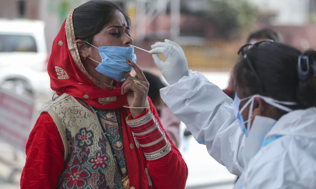 A health worker collects a swab sample from a woman to test for COVID-19 by a road side in Jammu, India, Monday, Dec.7, 2020. India is second behind the U.S. in total coronavirus cases but has one of the lowest deaths per million population globally. (AP Photo/Channi Anand)