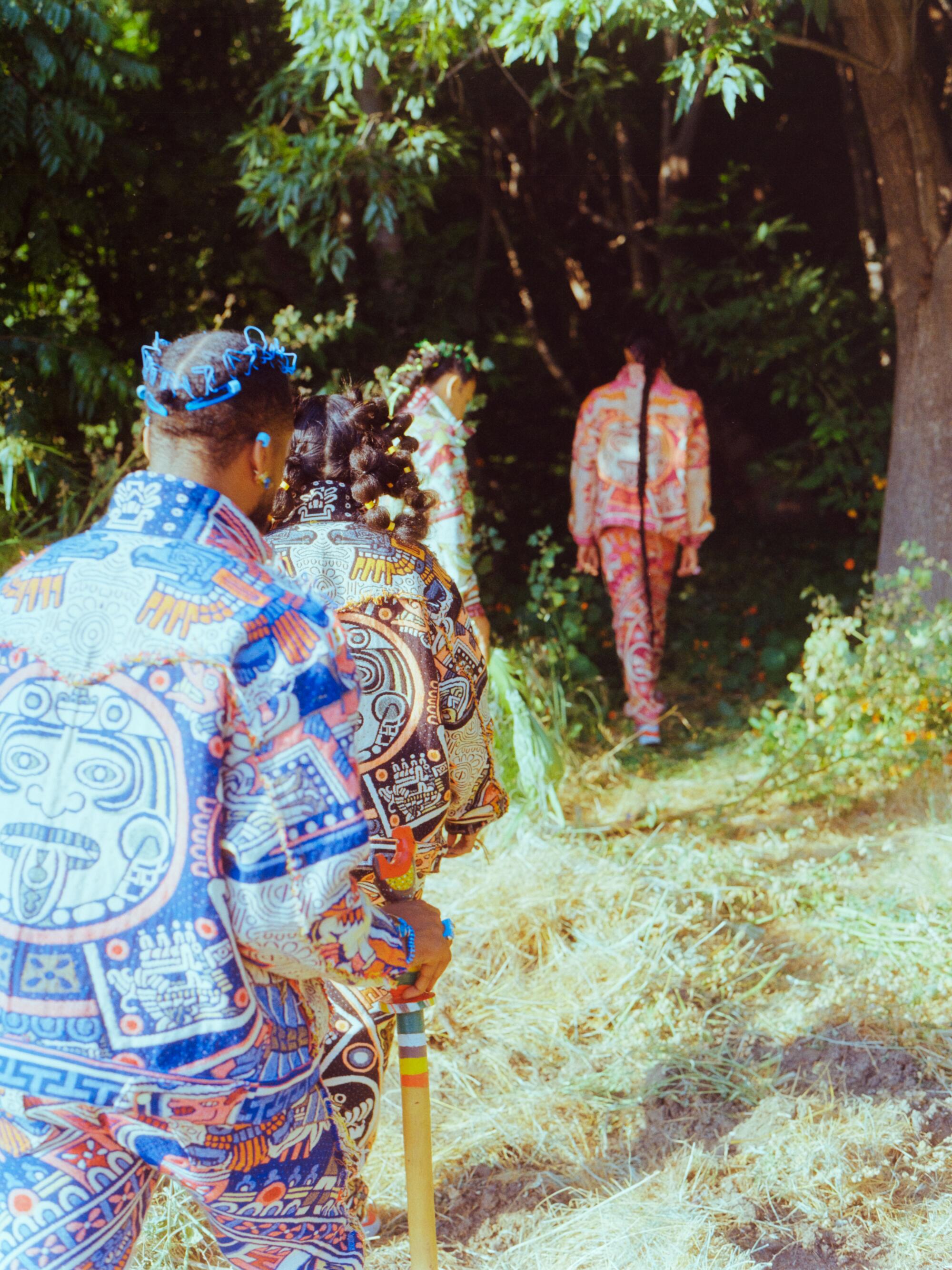 Four people in colorful outfits walk through an opening in the brush.