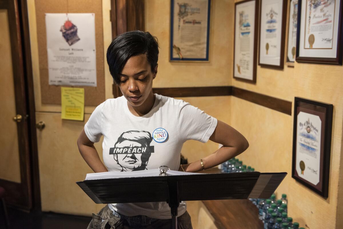 Actress Jazmyn Simon looks at a binder on a stand while wearing a white T-shirt with Trump's face on it and the word "impeach" across his eyes.
