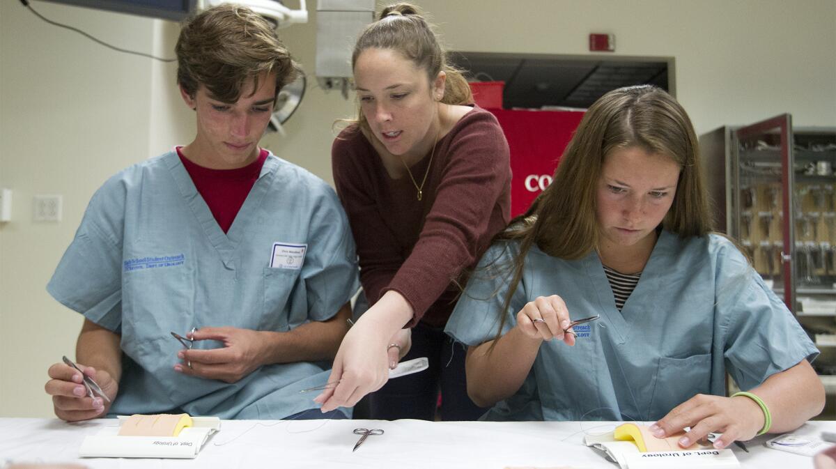 Simone Vernez, center, a UCI Medical student, trains Corona del Mar High School Future Doctors Club members Chris Wendland, left, and Parker Hoffman how to open suture using forceps and medical tweezers at UCI Medical Center in Orange on Tuesday.
