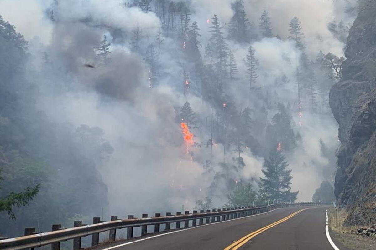Smoke and flames in a forested area next to a two-lane highway