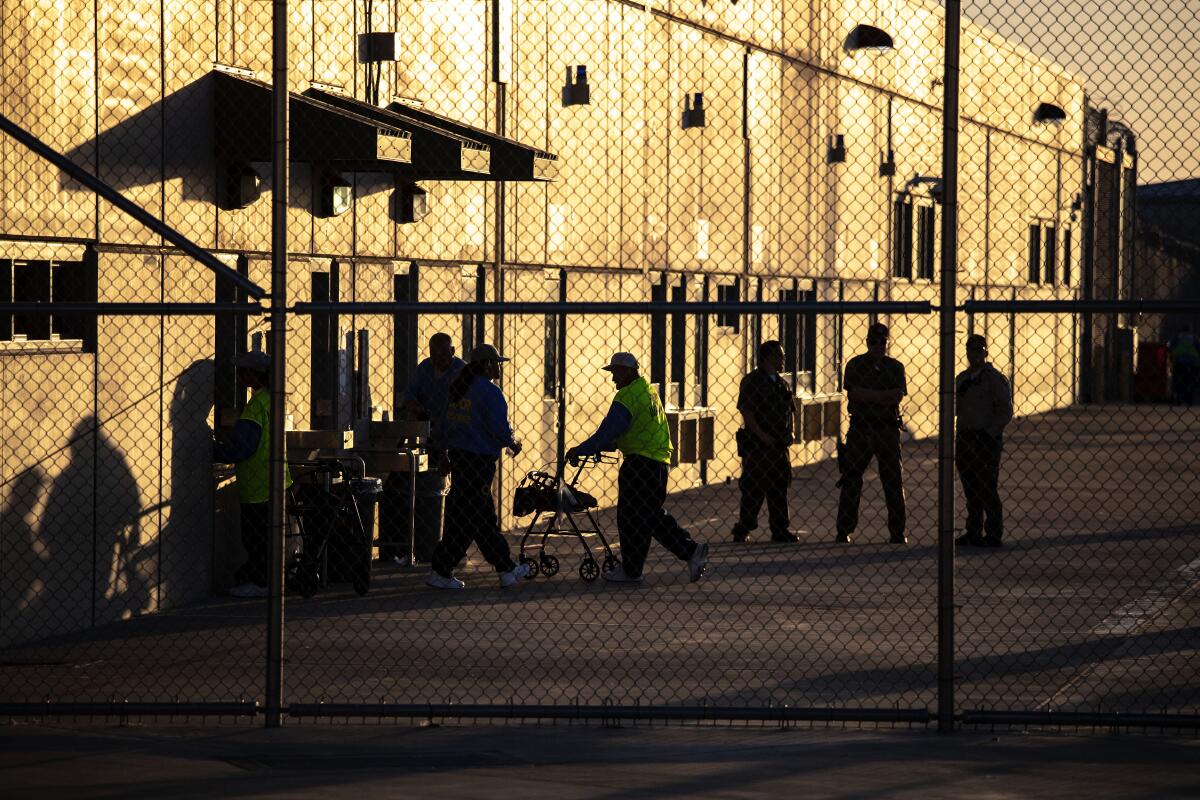 People stand in a yard next to a building behind a chain link fence.