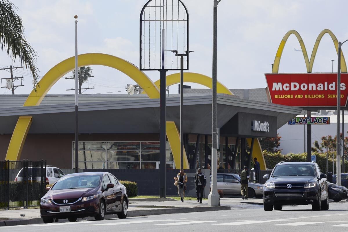 Cars and people outside a McDonald's restaurant where two gold arches appear to run through the roof