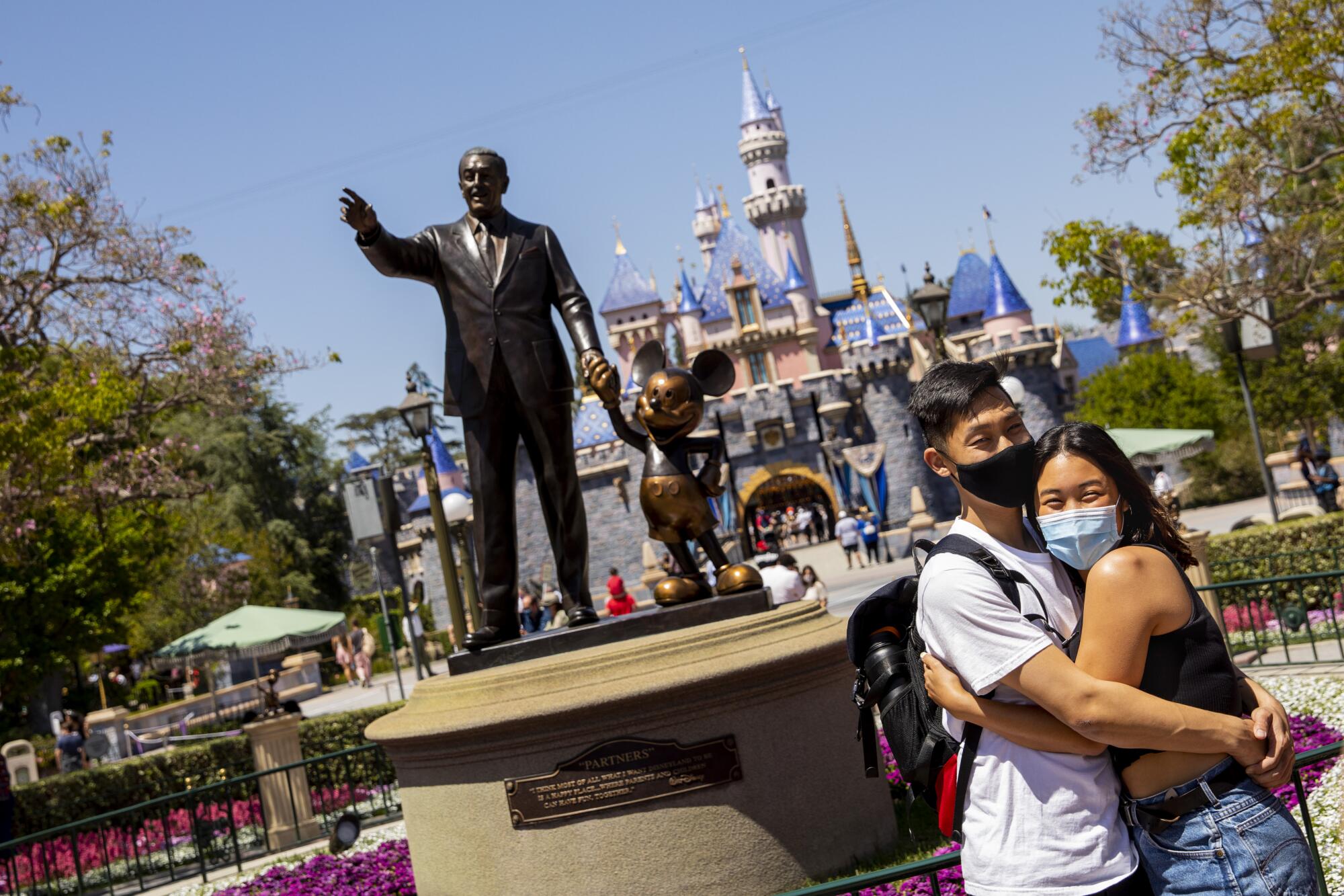 Two young adults hug in from of the Disneyland magic castle.