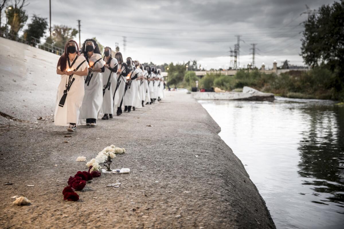 Artists dressed in white carry candles as they march along the banks of the river, where someone has placed flowers