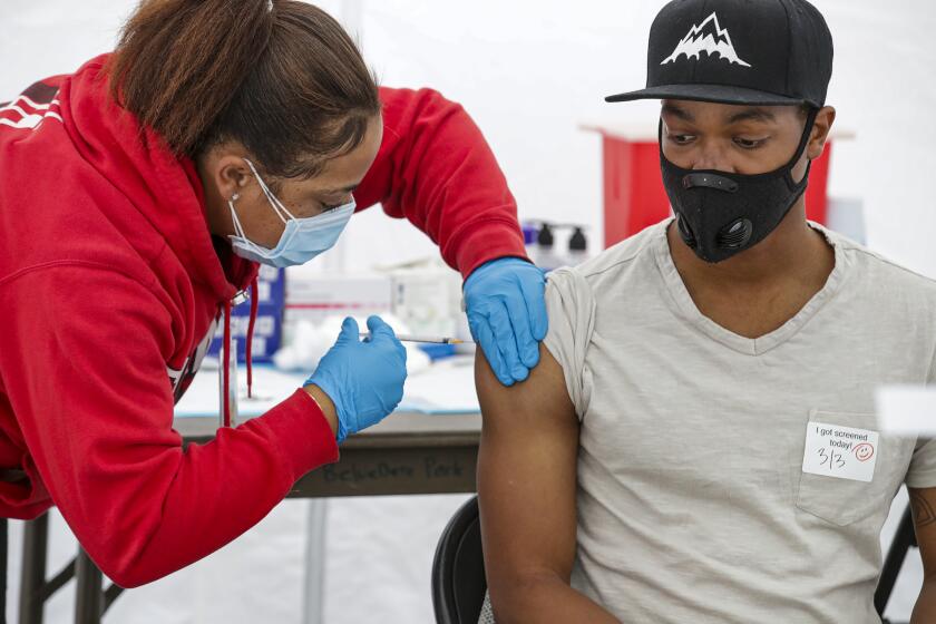 Los Angeles, CA - March 03: Keyaira Escoe, 20, left, a medical assistant, administers COVID-19 vaccine to Xavier Scott, 26, at a site opened by St. John's Well Child and Family Center at East Los Angeles Civic Center on Wednesday, March 3, 2021 in Los Angeles, CA.(Irfan Khan / Los Angeles Times)