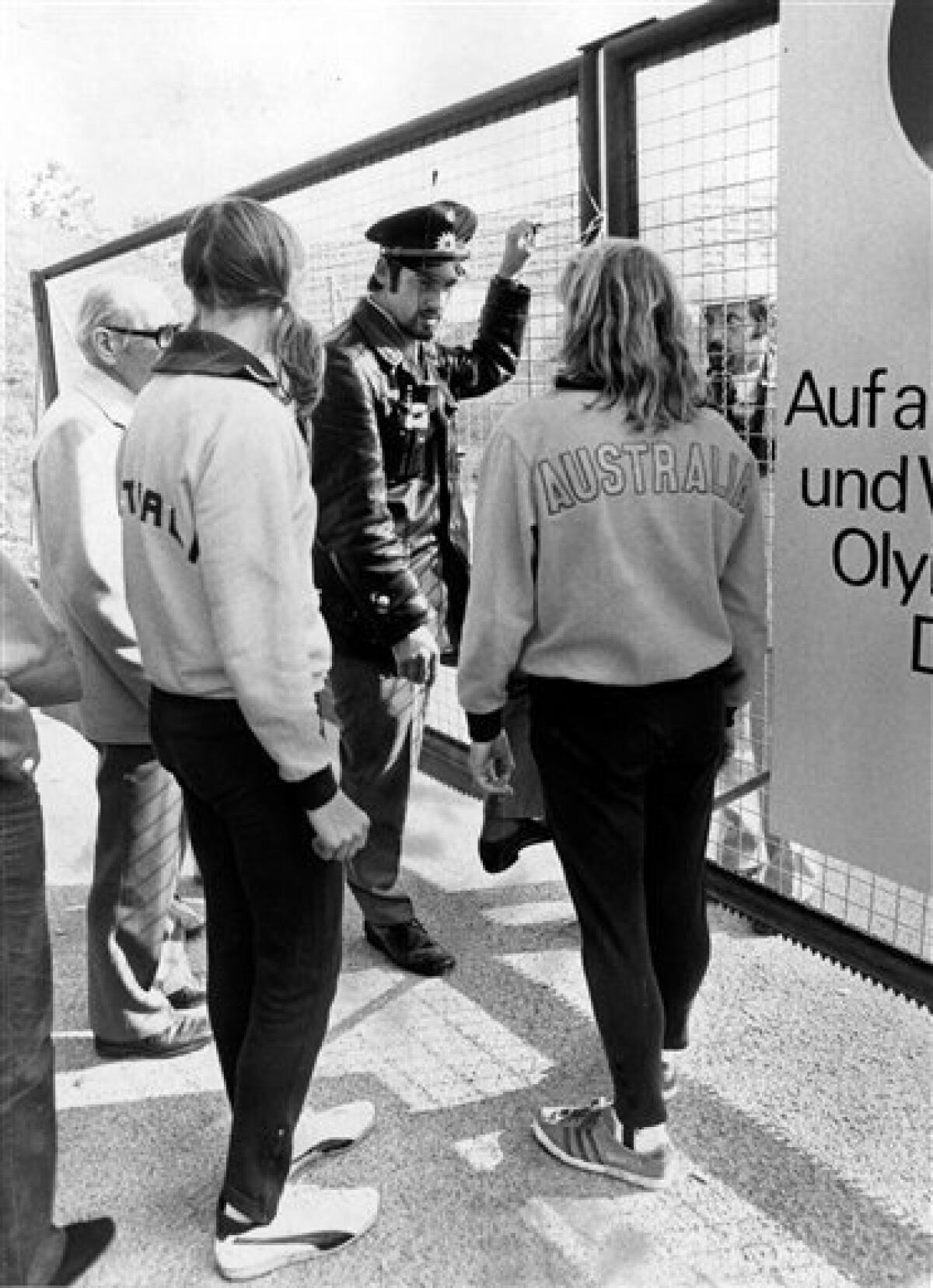 FILE - In this Sept. 5, 1972, file photo, a police officer blocks the entrance gate of the Olympic village in Munich, as two Australian athletes returning from early training try to get access. Doors were blocked following members of Israel's delegation taken hostage earlier. (AP Photo/File)