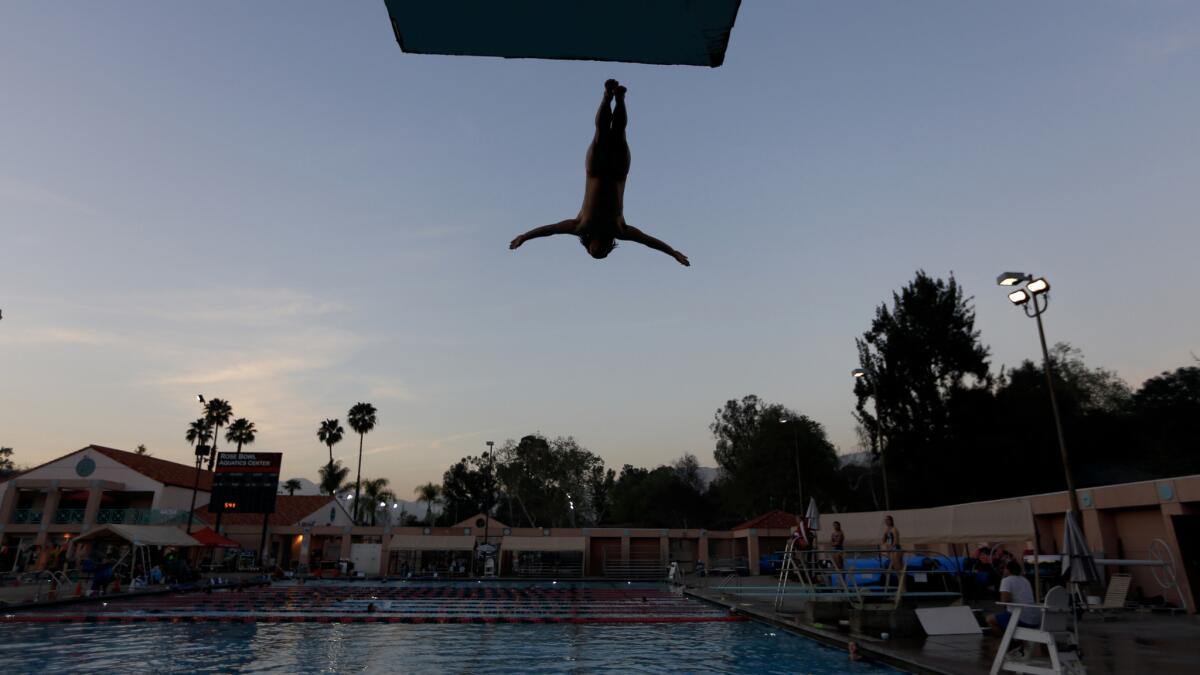 At dusk, Louis Morales of Pasadena dives in as his coach Lenny Larsen keeps a watchful eye on him at the Rose Bowl Aquatics Center in Pasadena.