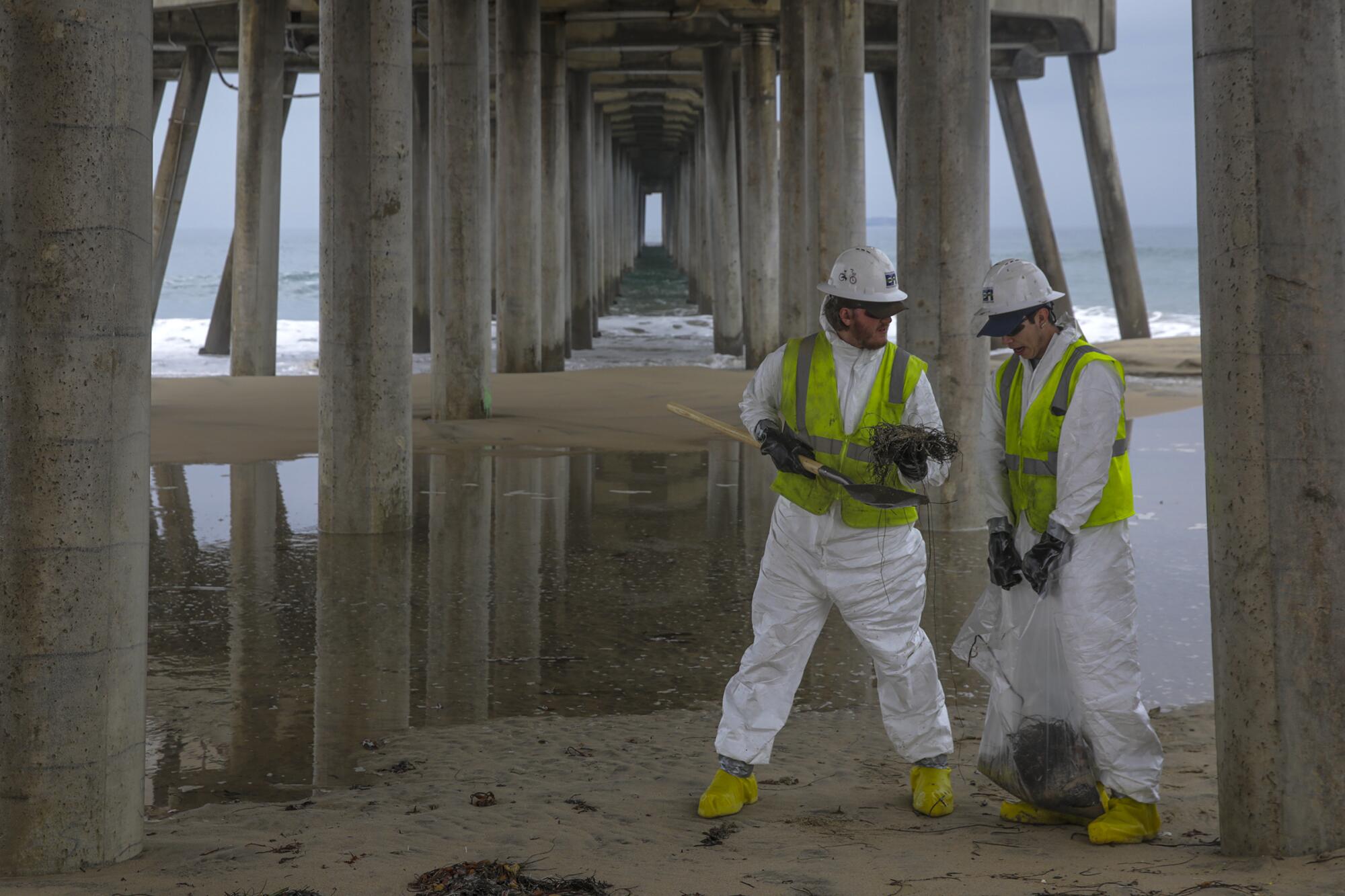 Two workers stand under a pier.
