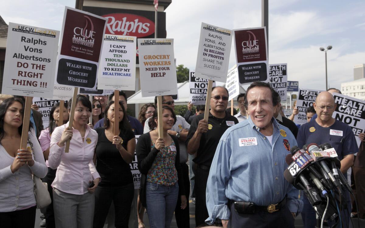 Workers carrying picket signs are behind a man wearing a blue shirt.