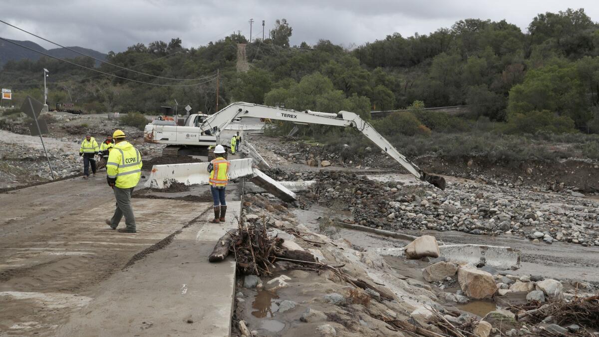 Crews use an excavator to remove large boulders and debris that were swept down Trabuco Creek from recent downpours on the Trabuco Canyon Road bridge earlier this month. Forecasters predict the Holy fire burn scar could see 2.5 to 6 inches of rain later this week.
