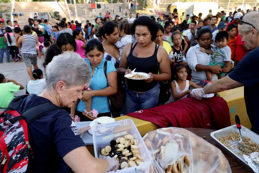 MATAMOROS, TAMAULIPAS -- TUESDAY, OCTOBER 1, 2019: Mayela Villegas, 26, of San Salvador, El Salvador, a transgender woman, fled her home after receiving death threats from gangs, lines up with other migrants from Central America and Mexico, awaiting the outcome of their U.S. immigration court cases in a tent encampment near the Gateway International Bridge, gather as volunteers dole out dinner at the U.S.-Mexico border in Matamoros, Tamaulipas, on Oct. 1, 2019. The stranded migrants seeking political asylum remain in Mexico under Trump administration’s “Remain in Mexico” policy. (Gary Coronado / Los Angeles Times)