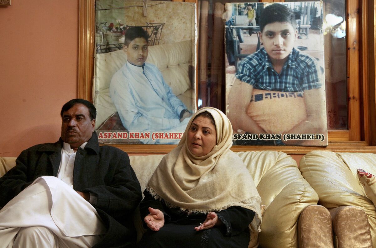 Pakistani mother Shahana with her husband Ajoon Khan sit next to photos of their son Asfand Khan, who was killed in a 2014 assault by Pakistani Taliban militants on an army public school, during an interview with The Associated Press, in Peshawar, Pakistan, Wednesday, Dec. 29, 2021. Each year on Jan. 17 Shahana bakes a cake and invites friends to her home to sing happy birthday, even light a candle but it's a birthday without the birthday boy, she says. (AP Photo/Muhammad Sajjad)