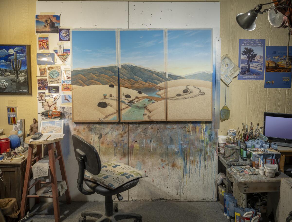 A landscape triptych hangs on the wall surrounded by paintings and other elements of a working studio. 